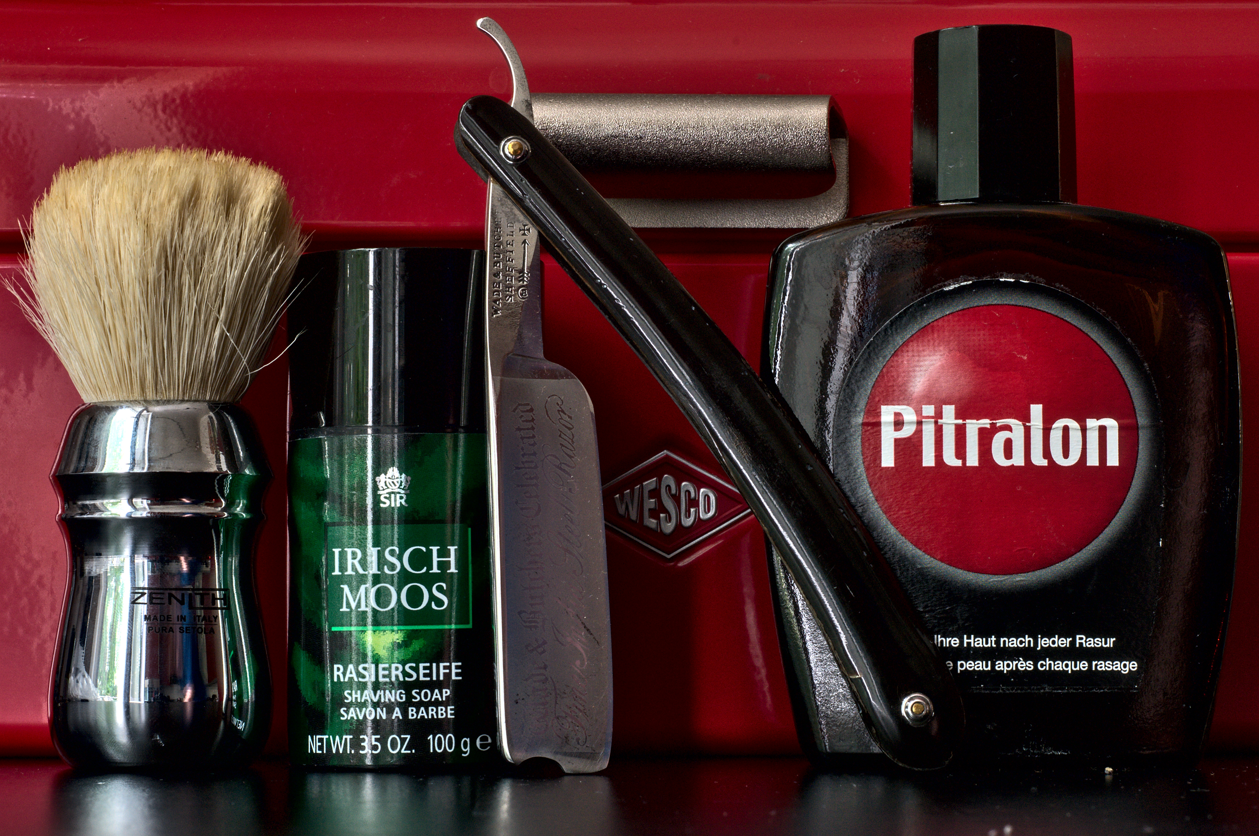 A Wade & Butcher Celebrated Fine India Steel Razor with original horn scales leaning against a stick of Sir Irisch Moos soap and a bottle of Swiss Pitralon splash next to a Zenith B21 brush